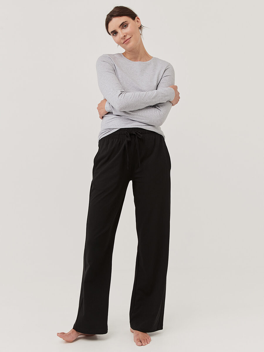 A model wearing a Pact long sleeve pajama set with a grey long sleeve top and black pants.