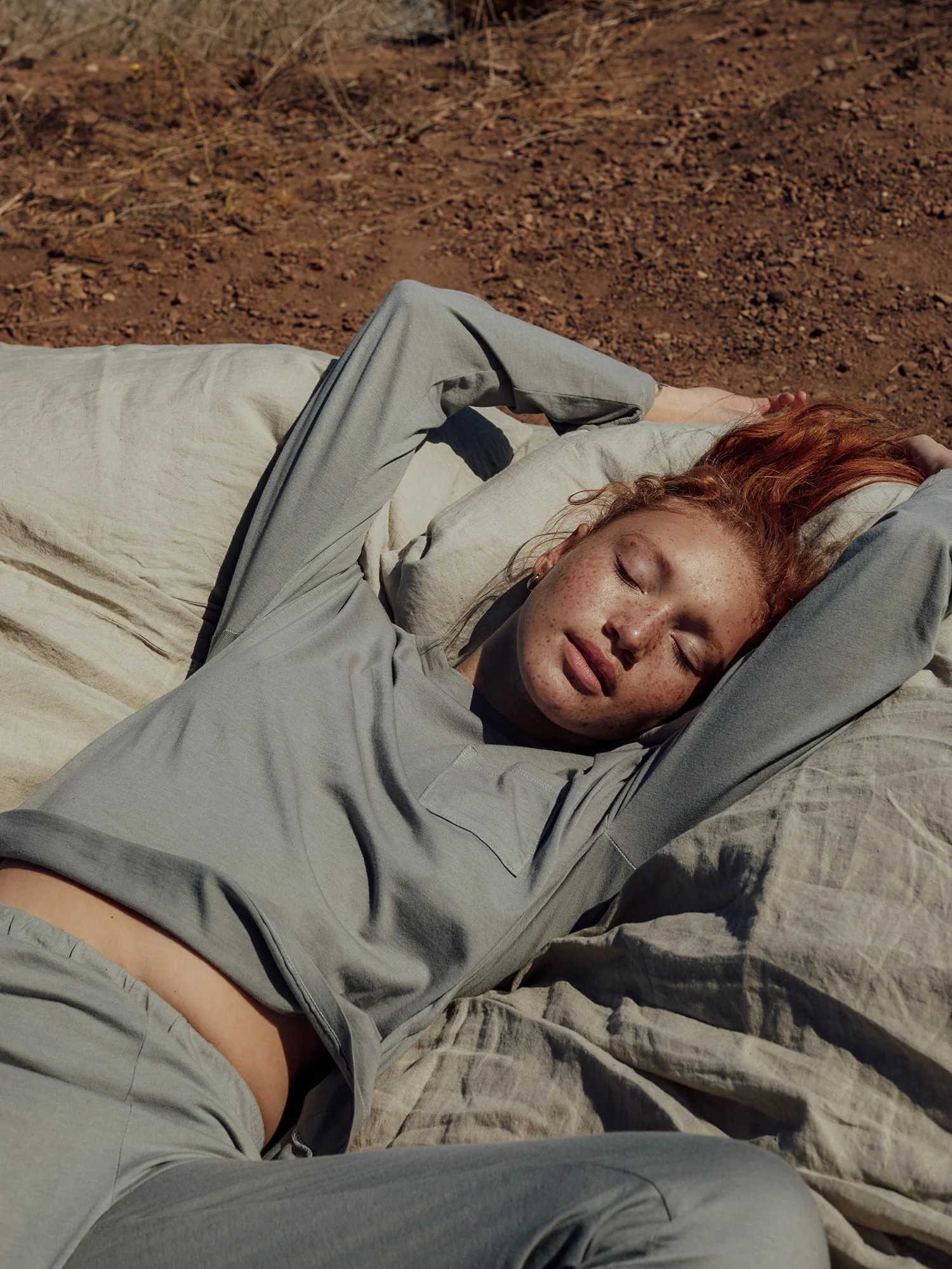 A model laying on a sage green comforter outside wearing Mate The Label's green long sleeve pajama set.